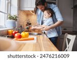 Kid, father and washing vegetables for cooking organic food, nutrition or learning healthy diet. Dad, happy child or cleaning carrot in kitchen for hygiene, wellness or teaching boy meal prep in home