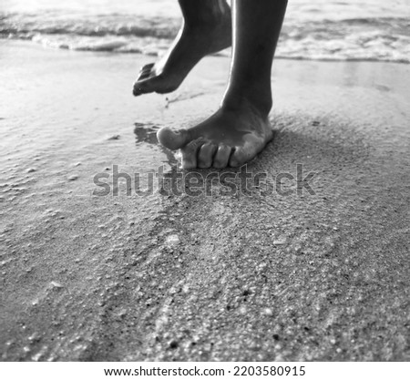 Kid feet walking on beach with lights and shadow and sea behind in black and white tones 