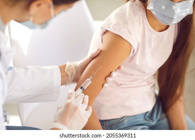 Kid Getting A Flu Shot At A Modern Clinic Or Hospital. Doctor Giving An Injection In The Arm To A Child In A Face Mask. Nurse Gives A New Effective Covid 19 Vaccine To A Little Girl, Close Up