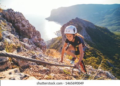Kid girl of 10 years old in helmet and special safety device equipment climbing high mountain via ferrata. Crimea.