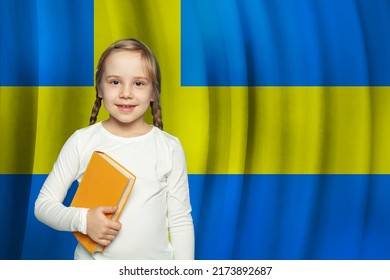 Kid girl with book standing against Swedish flag background. School and education in Sweden concept