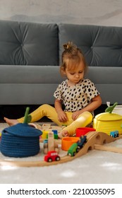 Kid Girl Builds A Toy Town And  Wooden Railway. A Little Girl Sitting On Floor Plays With Toy Train Locomotive,  Wooden Blocks And Toy Animals. Educational Game For Toddler In Modern Nursery.