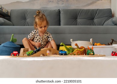 Kid Girl Builds A Toy Town And  Wooden Railway. A Little Girl Sitting On Floor Plays With Toy Train Locomotive,  Wooden Blocks And Toy Animals. Educational Game For Toddler In Modern Nursery.