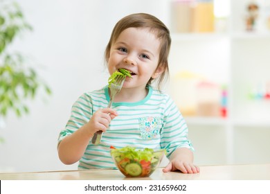 Kid Girl Eating Healthy Vegetables At Kitchen