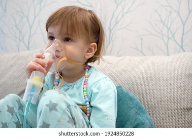 Kid Girl Makes Inhalation With A Nebulizer. Sick Child Holding Inhalator In Hand And Breathes Through An Inhaler At Home