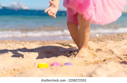 Kid girl on Easter egg hunt on the sandy beach. Happy Easter holidays concept 