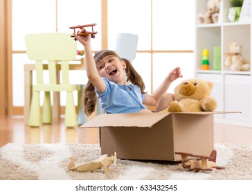 Kid Girl Playing Pilot Flying A Cardboard Box In Children Room