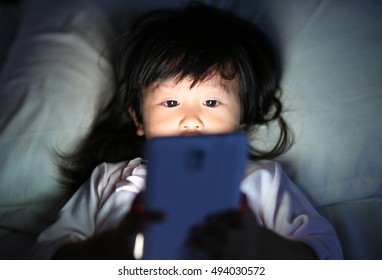 Kid Girl Playing Smartphone Lying On A Bed At Night