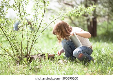 Kid girl playing with a tablet on a stump, spring, childhood outdoors, exploring nature - Powered by Shutterstock