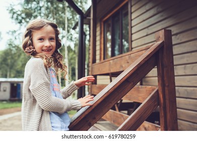 Kid Girl Playing At Wooden Cabin In The Woods. Child Spending Summer Vacation Outdoor At Country House