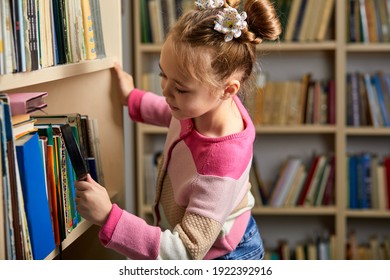 Kid Girl With Ponytails Choosing Books In Library After Classes, Enjoy Being Educated, Get New Information And Knowledge