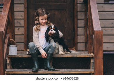 Kid Girl Relaxing With Her Spaniel Dog On Stairs At Brown Cabin In The Woods In Summer. 