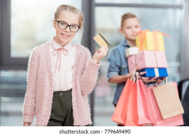 Kid In Glasses Holding Credit Card In Hand With Boy Holding Boxes On Background 