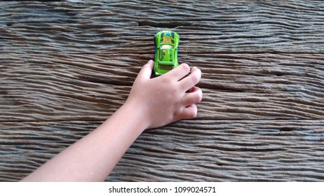 Kid Hand Hold Car Toy On Wooden Background. Blurr