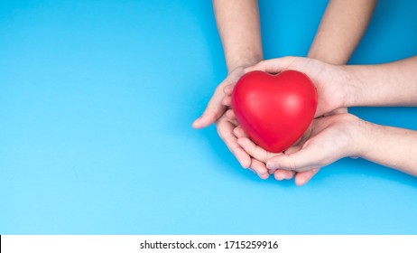 Kid Hand Hold Red Heart On Blue Background. Concept Donation Helps Find Loving Health Care Equity And Promote Well Being.  Top View.  Copy Space.  Gift For You.
