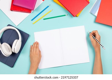 Kid hand holding pencil and writing in blank open notebook. Digital tablet, headphones, books, school stationary on blue background. Back to school, language learning, online classes, homeschooling - Powered by Shutterstock