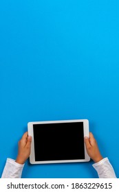 Kid Hand Holding White Digital Tablet Computer On Light Blue Background. Top View