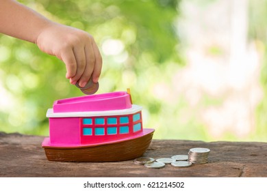 Kid Hand Putting A Coin Into A Pink Ship Bank. Saving And Investing Money Concept