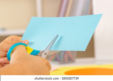 Kid Hands Cutting Light Blue Colored Paper With Scissors. Education, Learning, Paper Craft, Entertainment