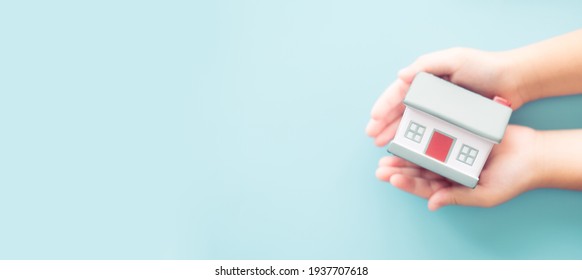 Kid hands holding home on blue banner background.Real estate, Family protection, Stay home Lockdown from Covid19 Coronavirus. Mortagage Crisis, Relocate Renovate Home.Family safety health.Refinance. - Shutterstock ID 1937707618