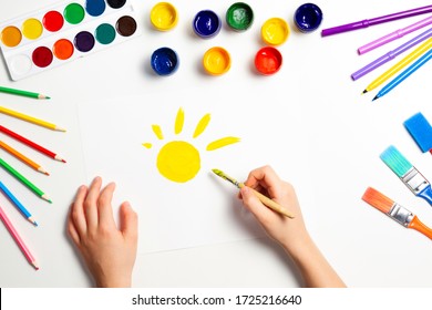 Kid Hands Painting Yellow Sun. Top View To White Table With Art Supplies