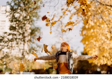 Kid Having Fun In Autumn Park With Fallen Leaves, Throwing Up Leaf. Child Boy Outdoors Playing With Maple Leaves