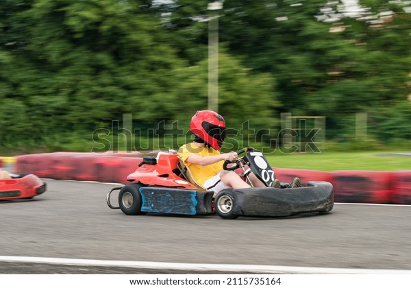 Kid in helmet fun racing go\
kart on an outdoor circuit with motion-blurred\
background