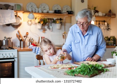 Kid Is Helping Grandmother To Cook Italian Pizza In Cozy Home Kitchen For Family Dinner. Cute Girl Is Cooking Homemade Food. Old Senior Woman Is Teaching Child. Children Chef Concept.