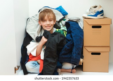 Kid Hiding Among Messy Clothes Inside Closet. Organization And Storage Of Clothes At Home. Mess In The Wardrobe. Boy With Messy Colorful Clothing At Room. Untidy Clutter Clothing Closet.