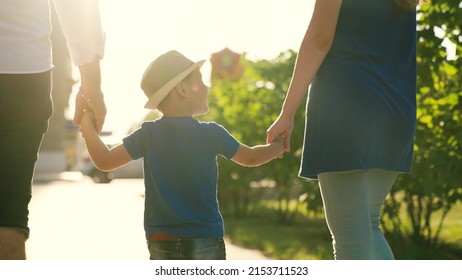 Kid holding hands, Mom dad son walking down street together. Happy family in Park at sunset. Teamwork. People on walk have fun. Family trip on foot. Happy family concept. Family game, parents son