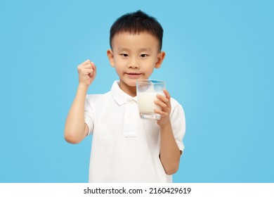 Kid Holding Milk Glass With Smile And Fist Up, Strong Gesture, Wearing White Shirt On Blue Background