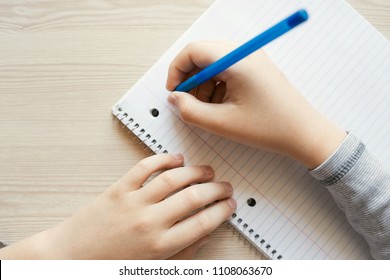 Kid holding pen and writing in notebook. Close up, top view.