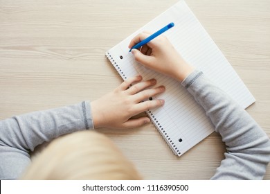 Kid holding pen and writing in notebook. Close up, top view.