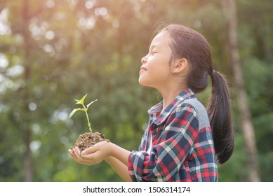 Kid Holding Young Plant In Hands Against Spring Green Background. Environment Earth Day In The Hands Of Trees Growing Seedlings. Concept Ecology