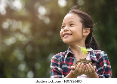 Kid Holding Young Plant In Hands Against Spring Green Background. Environment Earth Day In The Hands Of Trees Growing Seedlings. Concept Ecology