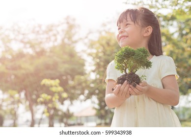 Kid holding young plant in hands against spring green background. Ecology concept