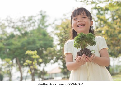 Kid Holding Young Plant In Hands Against Spring Green Background. Ecology Concept