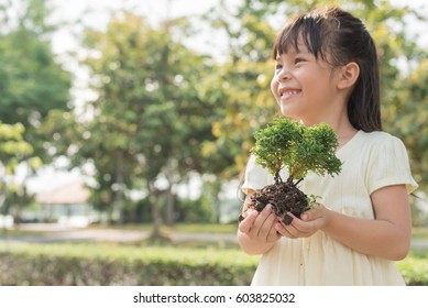 Kid Holding Young Plant In Hands Against Spring Green Background. Ecology Concept