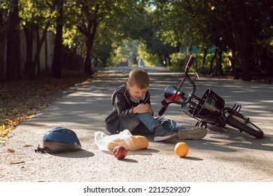 Kid Hurts His Knee After Falling Off His Bicycle.when He Fell, He Scattered His Purchases On The Ground. The Boy Hit His Head On The Asphalt