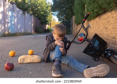 Kid Hurts His Knee After Falling Off His Bicycle.when He Fell, He Scattered His Purchases On The Ground. The Boy Hit His Head On The Asphalt