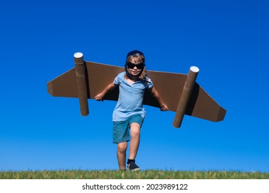 Kid With Jet Pack Superhero. Child Pilot Against Summer Sky Background. Boy With Paper Plane Flight, Toy Airplane With Cardboard Wings, Imagination, Kids Freedom.