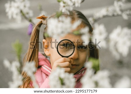 Kid learning about environment. Natural education activity for World Earth day. Exploring in spring, blooming flowers in the garden. Serious girl looking though the magnifying glass