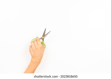 Kid Left Hand Holding Scissors Over White Background. Top View, Copy Space For Text. Left Handers Day