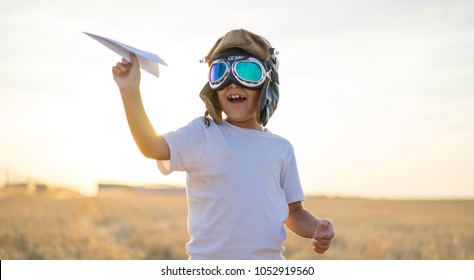 Kid, Little Boy Wearing Helmet And Dreams Of Becoming An Aviator While Playing A Paper Plane At Sunset