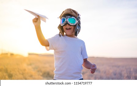 Kid, Little Boy Wearing Helmet And Dreams Of Becoming An Aviator While Playing A Paper Plane At Sunset