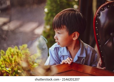 Kid Looking Out Window. Adorable Little Caucasian Kid Boy Stand Still Near Window Glass And Looking To Outside Alone During Bright Sunny Day. Little Child Reflecting Bored And Loneliness At Home