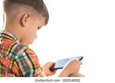 The kid looks into the mobile while sitting in the summer on the street. Small child with a phone in his hands.