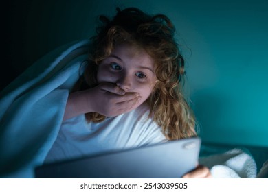 Kid lying on bed and surfing Internet on tablet in dark room. Boy reading Tablet in bed at night. Kid in pajamas using tablet before going to bed. Kid using gadgets. Child watching his tablet in bed. - Powered by Shutterstock