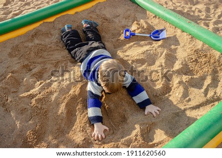 The kid is lying on his stomach in the sand in the city playground.