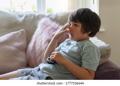 Kid Lying On Sofa Scratching His Nose While Watching TV,  Child Feeling Itchy On His Nose From Fluffy Cushion, Young Boy Relaxing At Home On His Own In Weekend. Positive Children Concept